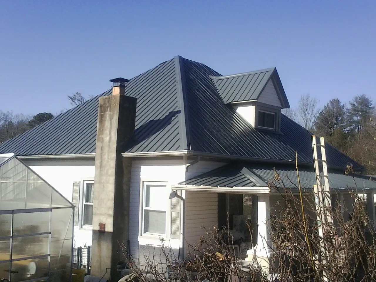 Dark blue standing seam metal roof on a white farmhouse with dormer — Slate & Tile Roof Repair by Roofing Brothers in Shenandoah Junction