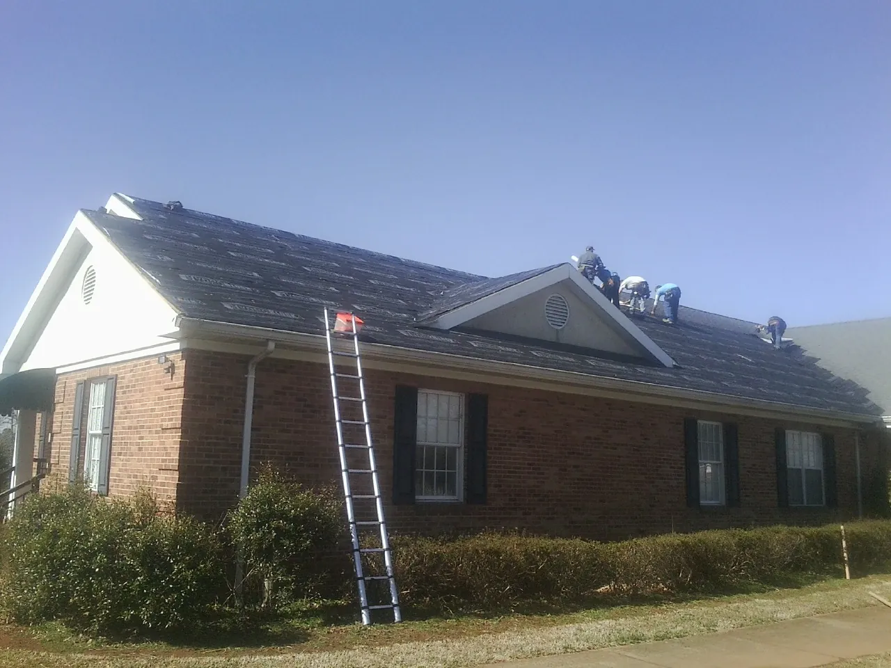 Crew tearing shingles off a brick ranch roof with a ladder set — Emergency Roof Repair work by our crew in Shenandoah Junction