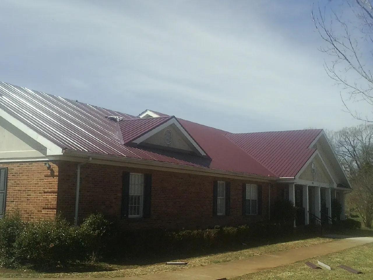 Red metal roof with gabled entries on a long brick building, from a Hail Damage Roof Repair job in Shenandoah Junction