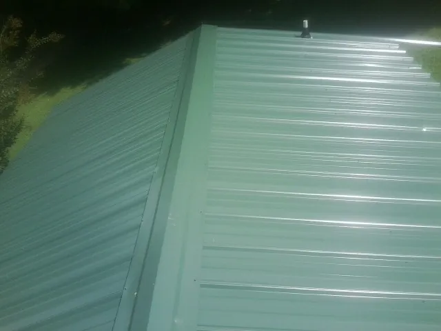 New green metal panels meeting at the ridge of a roof — Flat Roof Repair work by our crew in Shenandoah Junction