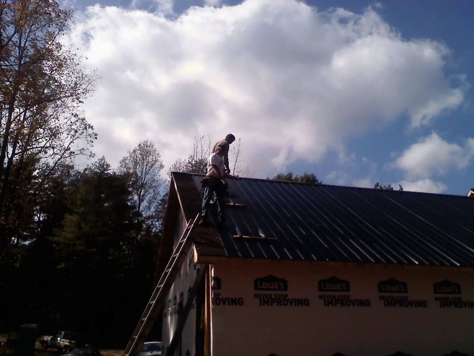 Roofer fastening dark metal panels high against a cloudy sky, from a Roof Inspection job in Shenandoah Junction