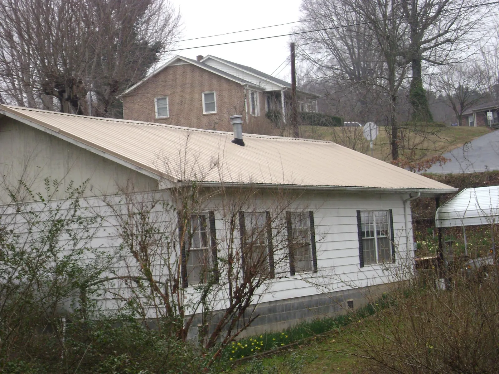 Tan metal roof on a white sided house set into a hillside — Commercial Roofing by Roofing Brothers in Shenandoah Junction